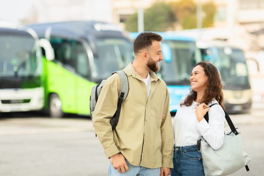 Happy man and woman with backpacks smiling at each other, ready to board a bus for a trip, enjoying travelling together
