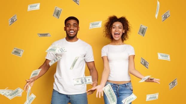 Young black couple standing under money banknotes shower