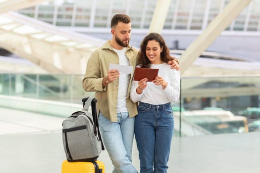 A man and woman walk beside their luggage, looking at papers together, possibly preparing for a trip.