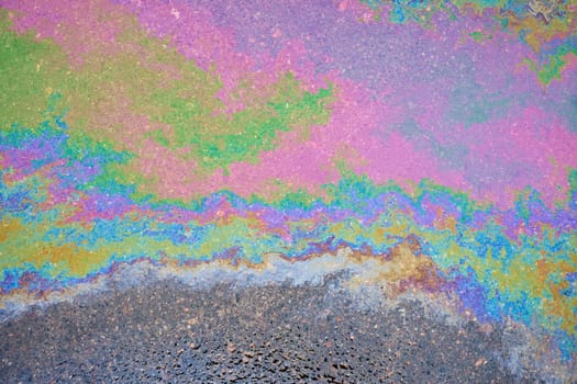 Oil stains from leaks in the car engine. Oil after rain makes spots with rainbow reflections refractive sun spectrum.