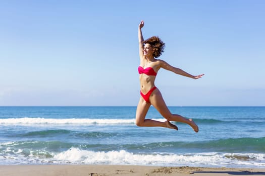 Slim woman in bikini jumping on sandy beach
