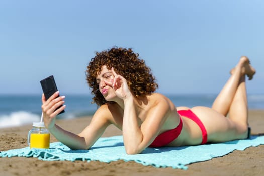 Cheerful woman in bikini taking selfie on beach
