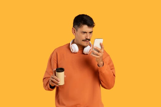 Focused man examining smartphone with coffee in hand