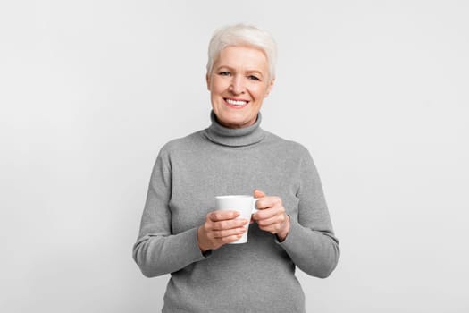 Elderly woman happily holding a white cup