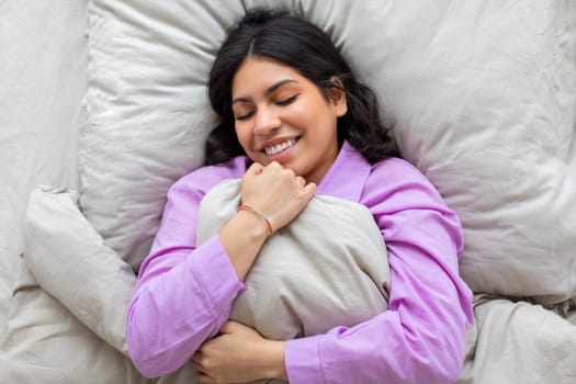 Woman hugging pillow while smiling on bed