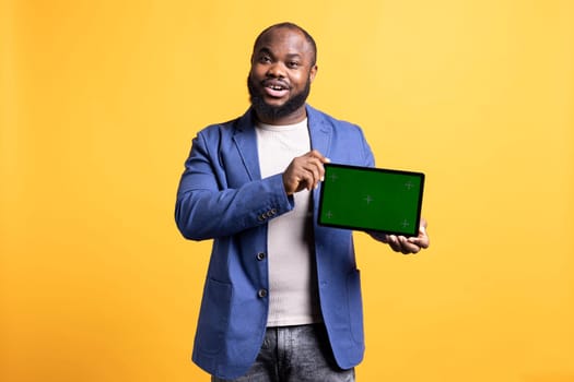 Jolly man presenting video on green screen tablet, studio background