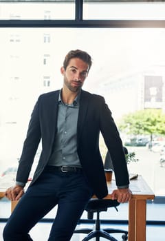 Portrait, business and man lean on desk in modern office with city view of New York and professional. Male corporate manager or supervisor for company and agency, workplace and career in operations