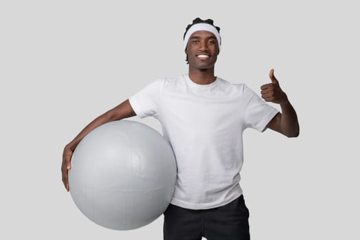 Smiling man holding fitness ball giving thumbs up