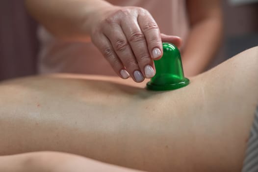 A woman undergoes an anti-cellulite massage procedure using a vacuum jar. Close-up of the lower back.