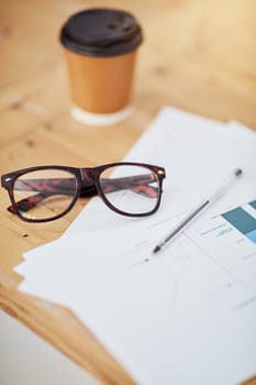 Glasses, coffee cup and documents with charts, graph and financial report for accountant on desk in office. Spectacles, disposable drink and paperwork for business statistics and finance review