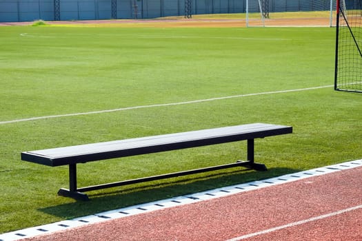 Empty bench on the sports field with green grass and red running track