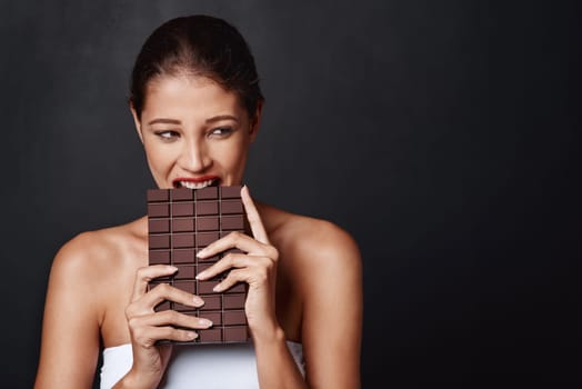 Chocolate, dessert and woman in studio eating for unhealthy diet, craving sugar or cheat meal on dark background. Bite, calories and female model for snack temptation, sweet addiction or cacao candy