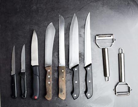 Knives, tools and kitchen equipment on table for professional chef, restaurant and culinary steel. Instrument, cutlery and blade for gourmet cafe, cutting and catering service in studio for meal prep