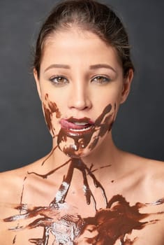 Woman, licking lips and chocolate on body for temptation, sweet craving and messy paint. Young person with guilty facial expression and isolated for candy, brown sauce and sugar for delicious tasty