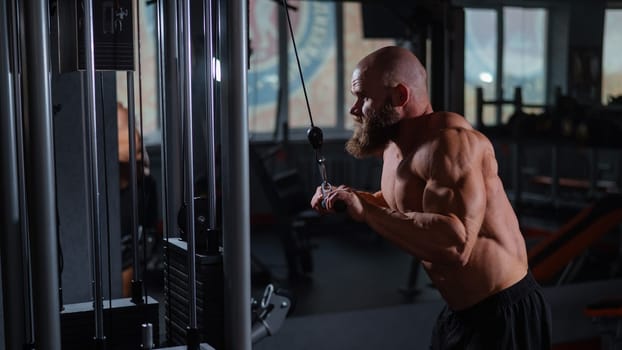 Bald Caucasian Bodybuilder doing heavy triceps exercises with cable.