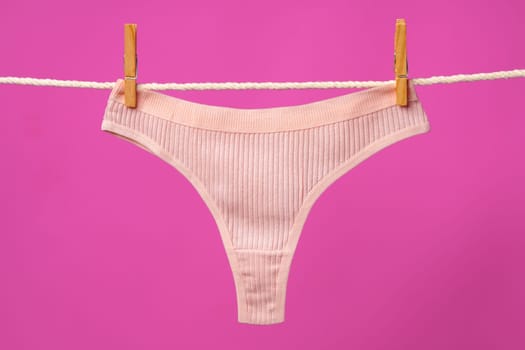Female panties hanging on rope against pink studio background