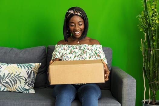 African young woman sit on couch at home unpack cardboard box with online purchase