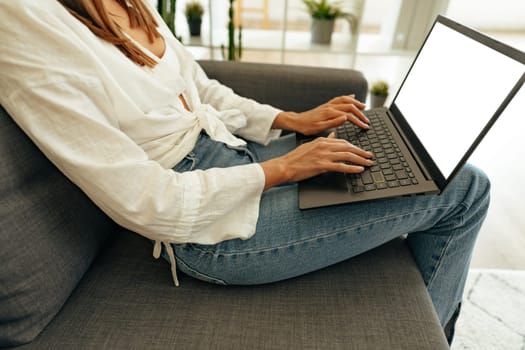Woman using laptop computer while sitting on a sofa at home.