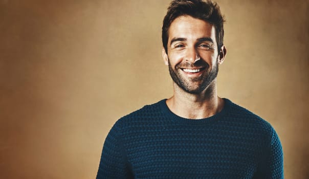 Smile, portrait and man with clothes for fashion, style and casual wear isolated on brown background. Face, happy or model with trendy sweater, closeup and cool person in studio backdrop with mockup