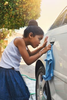 Young, girl and car in cleaning with cloth in outdoor for carwash at home for chores or helping. Female child, washing and vehicle in yard for responsibility, childhood and development in working