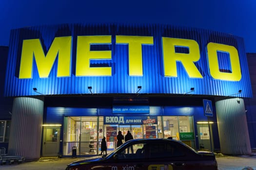 Tyumen, Russia-March 02, 2024: Metro sign glows brightly, with the silhouettes of city buildings in the background.