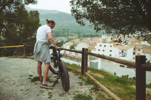 Young male traveler standing beside bicycle and happy for view of the nature and city in mountains on background