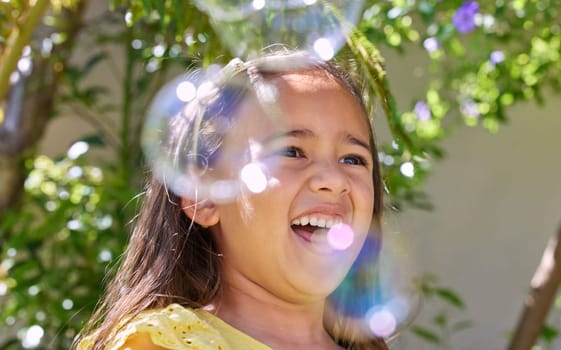 Girl, child and happy with bubbles in garden for playing, excited or outdoor on vacation in summer. Kid, smile and soap for funny game in backyard, spring or sunshine by trees on holiday in Colombia
