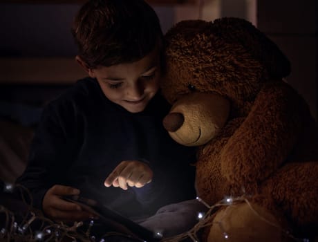 Tablet, teddy bear and boy child at night watch movie, film or show online for entertainment at home. Relax, dark and young kid streaming video on internet with digital technology in bedroom at house