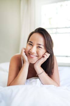 Morning, portrait and happy woman wake up in bed on holiday or relax on vacation with a smile. Healthy, rest and Asian girl with positive attitude ready to start weekend with wellness in home