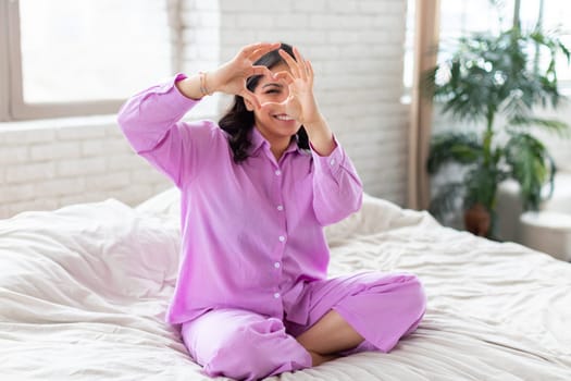 Woman in lilac pajamas sitting on bed
