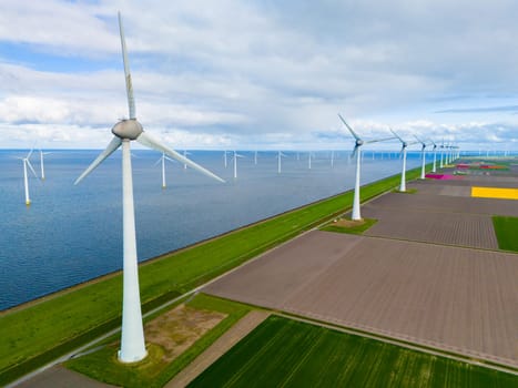 A mesmerizing aerial view of a wind farm near the ocean, where giant turbine blades spin gracefully against the backdrop of the water in the Noordoostpolder Netherlands