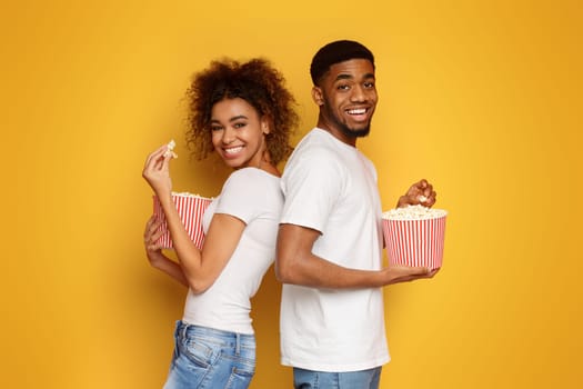 Man and woman eating popcorn on orange background