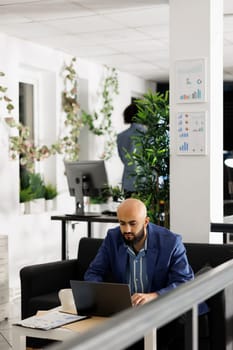 Arab businessman solving marketing strategy problems on laptop while working in start up business office room. Man entrepreneur developing product sales plan on computer in green open space