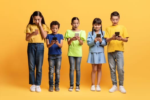 Shocked kids looking at cell phone screens, yellow background