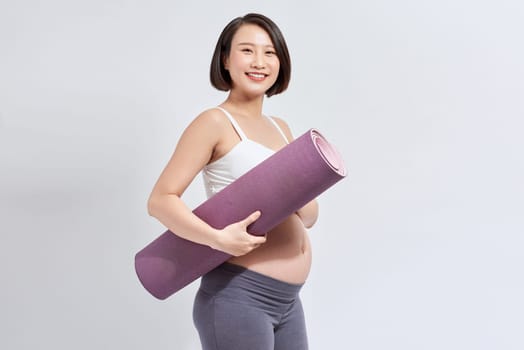 Portrait of a young pregnant woman holding a yoga mat in the studio on a white background