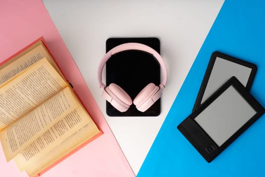 E-book reader, digital tablet with headphones and book on color paper background studio photo