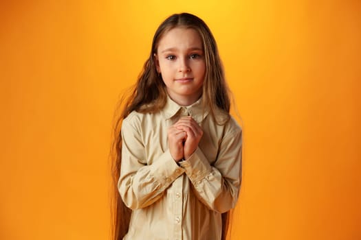 Little girl begging looking at viewer against yellow backgorund in studio