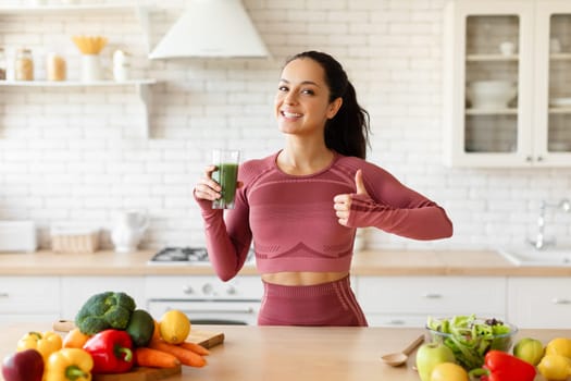 Lady Holding Green Smoothie And Gesturing Thumbs Up At Kitchen