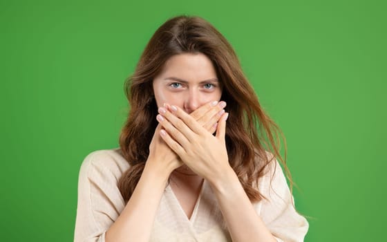 Serious young european woman in casual closes mouth with hands, keeps secret