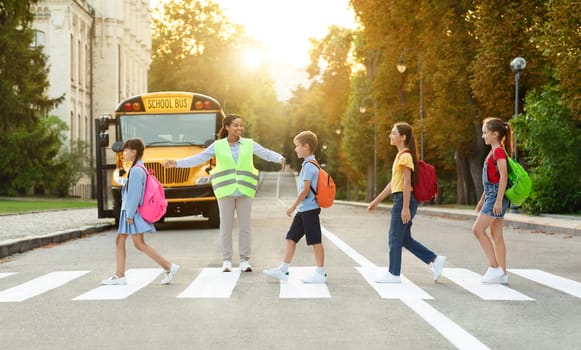 Group of children passing crosswalk on their way to school bus, diverse pupils cross the street with the crossing guard blocking traffic, boys and girls going home after classes, copy space