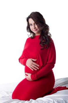 Pretty expectant mother sitting on bed in studio