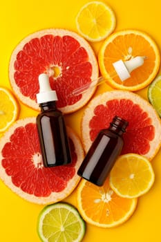 Citrus essential oil bottle on yellow background with sliced citrus fruits top view