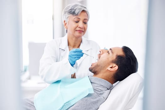 Woman, dentist and check teeth of man with tools for dental cosmetics, healthcare assessment and medical consulting. Patient, tooth and oral cleaning with mirror, excavator and orthodontic surgery