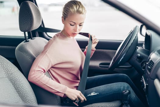 Beautiful woman fastening seat belt in small personal car.