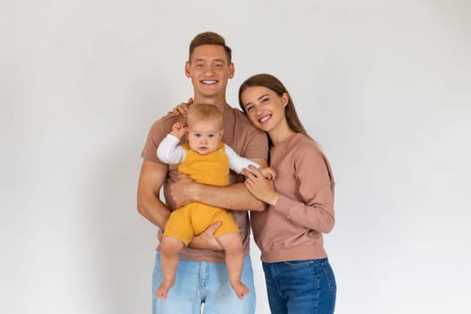 Happy Family Of Three With Cute Infant Baby Posing Over White Background