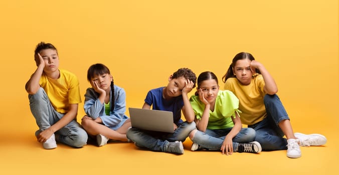 Bored diverse school aged kids sitting on floor with laptop