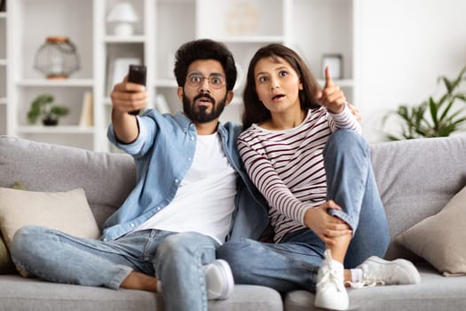 Amazed millennial couple sitting on couch at home, watching TV