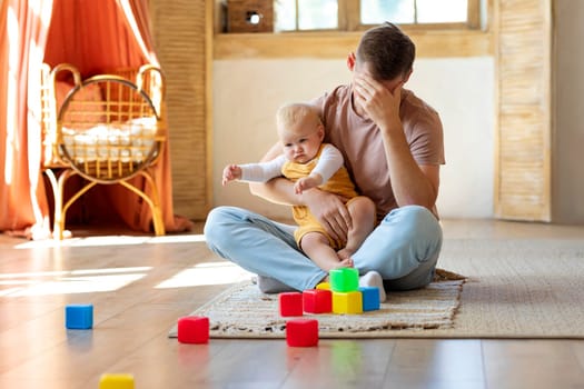 Exhausted Young Father Taking Care About Toddler Baby At Home