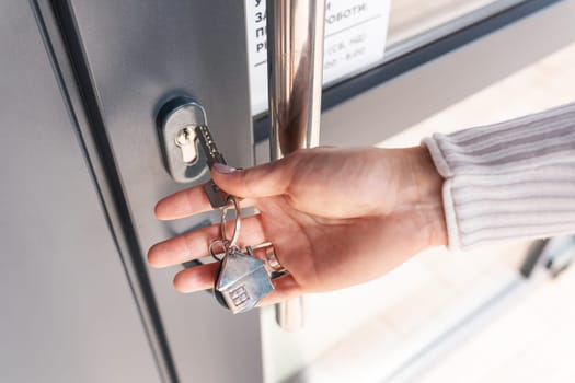A woman's hand opens the door with a key on which the keychain hangs at home.
