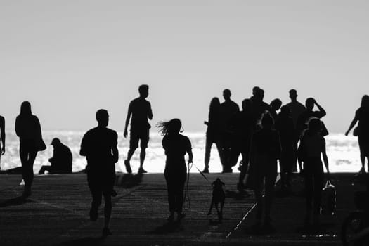 Monochrome shot of silhouettes of people walking on the hill by the sea